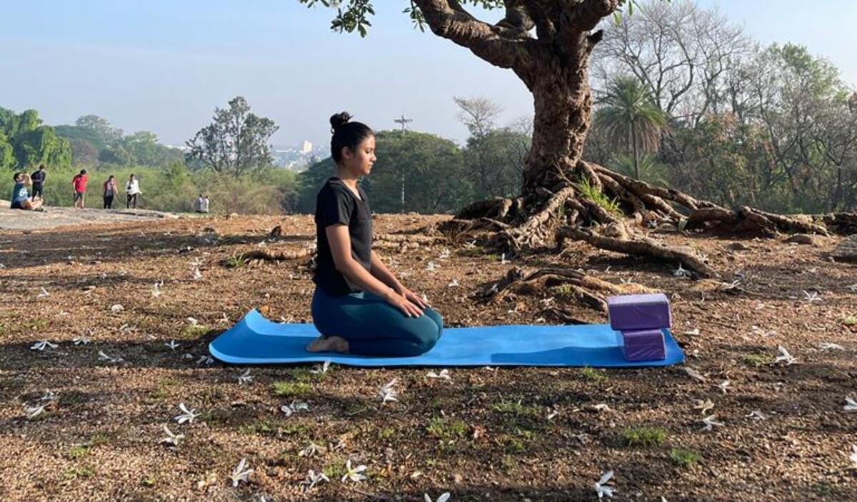 Medha in a seated, calming yoga pose under a tree